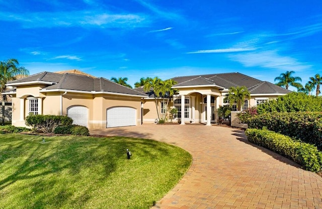 mediterranean / spanish-style home featuring a tile roof, decorative driveway, a front lawn, an attached garage, and stucco siding