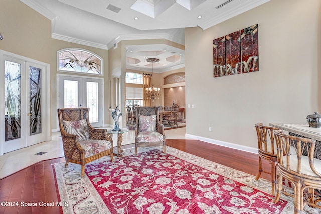 living area featuring a towering ceiling, french doors, hardwood / wood-style flooring, a notable chandelier, and ornamental molding