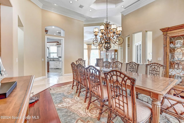 dining space with a towering ceiling, a notable chandelier, ornamental molding, and light wood-type flooring