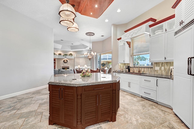 kitchen featuring recessed lighting, dark stone counters, a raised ceiling, a sink, and a notable chandelier