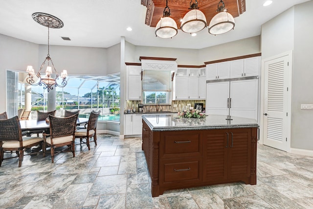kitchen with a kitchen island, a notable chandelier, tasteful backsplash, and stone tile flooring