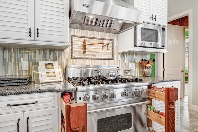 kitchen featuring wall chimney range hood, decorative backsplash, appliances with stainless steel finishes, white cabinets, and dark stone counters