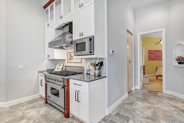 kitchen featuring ceiling fan, white cabinetry, dark stone countertops, wall chimney exhaust hood, and stainless steel appliances