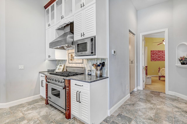 kitchen with glass insert cabinets, baseboards, wall chimney exhaust hood, stone finish flooring, and appliances with stainless steel finishes
