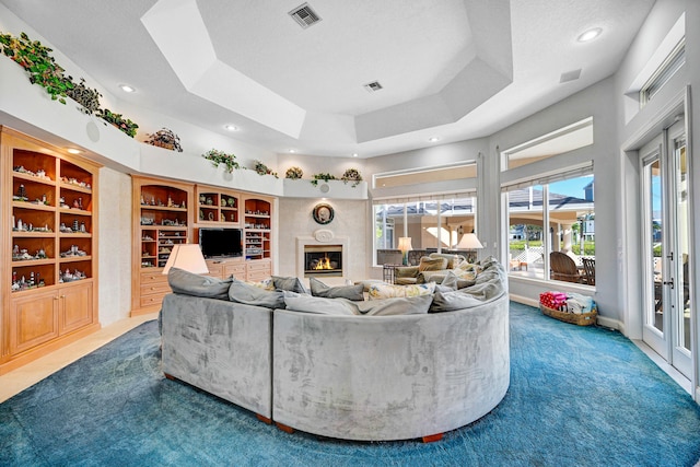 carpeted living room featuring a textured ceiling, built in shelves, and a raised ceiling