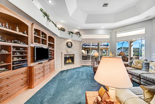 carpeted living area with visible vents, a high end fireplace, a raised ceiling, a high ceiling, and recessed lighting
