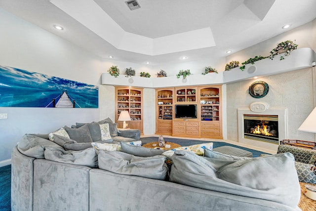 living room featuring visible vents, built in features, a glass covered fireplace, recessed lighting, and a tray ceiling