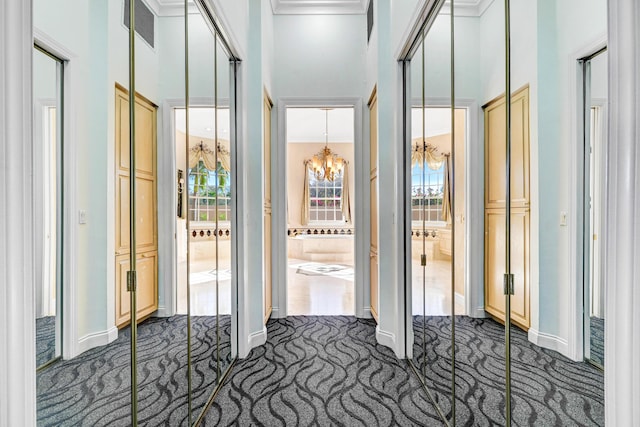 hallway with dark carpet, baseboards, a high ceiling, and a notable chandelier