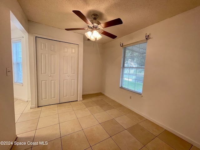 unfurnished bedroom featuring multiple windows, light tile patterned floors, a closet, and ceiling fan