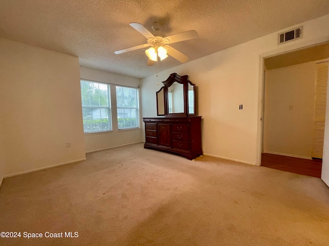 unfurnished bedroom featuring ceiling fan, light colored carpet, and a textured ceiling