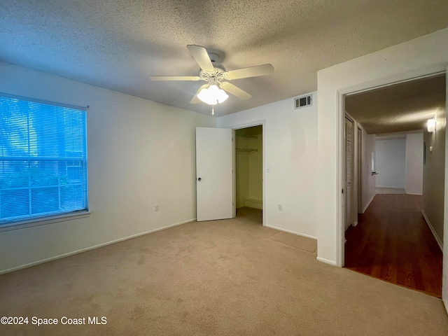 unfurnished bedroom with ceiling fan, a spacious closet, light colored carpet, a textured ceiling, and a closet