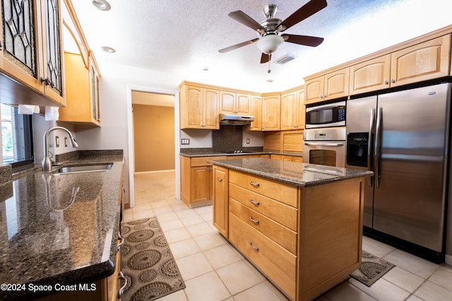 kitchen with sink, a center island, dark stone counters, ceiling fan, and stainless steel appliances