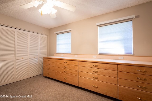 unfurnished bedroom with light carpet, ceiling fan, a closet, and a textured ceiling