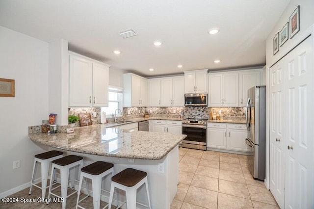 kitchen with tasteful backsplash, appliances with stainless steel finishes, a peninsula, white cabinets, and a sink