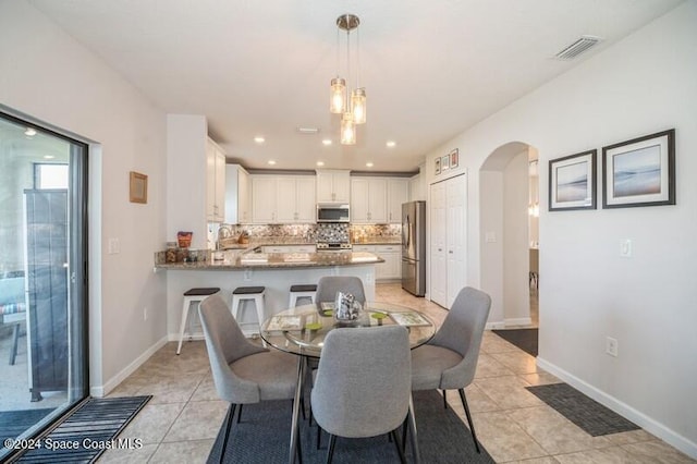 dining space with light tile patterned floors, visible vents, arched walkways, and baseboards