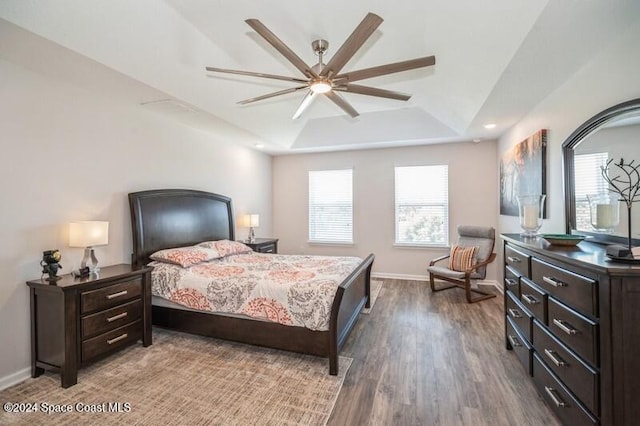 bedroom with ceiling fan, baseboards, a tray ceiling, and wood finished floors