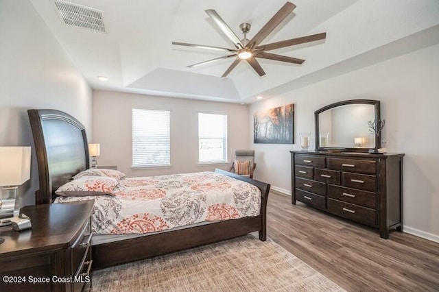 bedroom featuring visible vents, a raised ceiling, baseboards, and wood finished floors