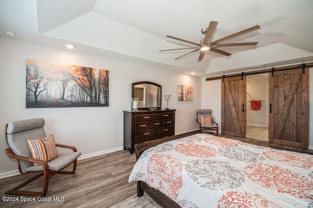 bedroom featuring a raised ceiling, a barn door, wood finished floors, and baseboards