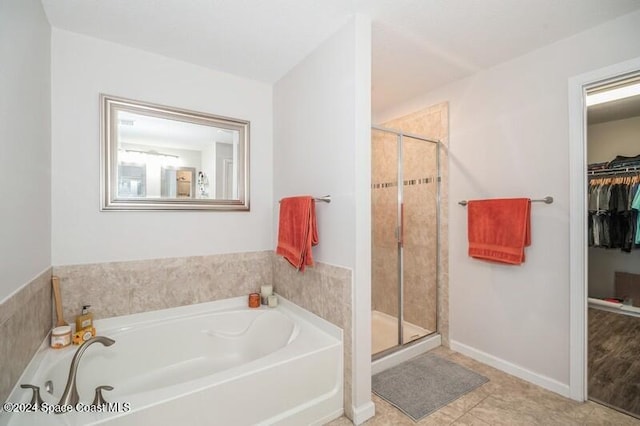 bathroom featuring a stall shower, baseboards, a walk in closet, and a garden tub