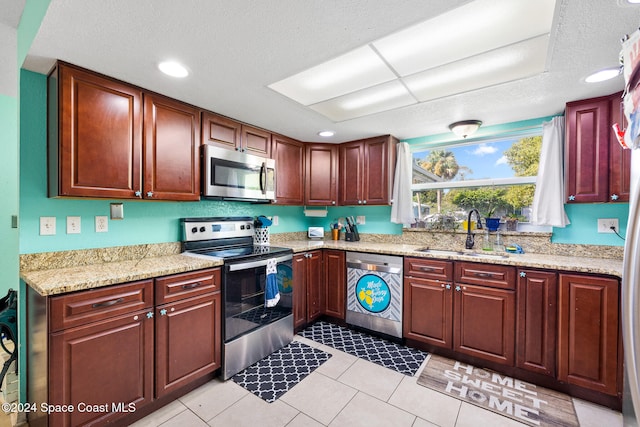 kitchen with light stone counters, appliances with stainless steel finishes, a textured ceiling, light tile patterned flooring, and sink