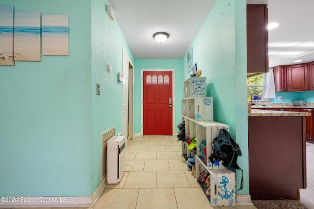 doorway with a textured ceiling and light tile patterned flooring