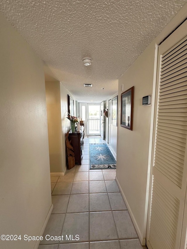 corridor with a textured ceiling and light tile patterned floors