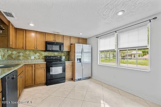 kitchen featuring sink, a textured ceiling, decorative backsplash, light tile patterned flooring, and black appliances