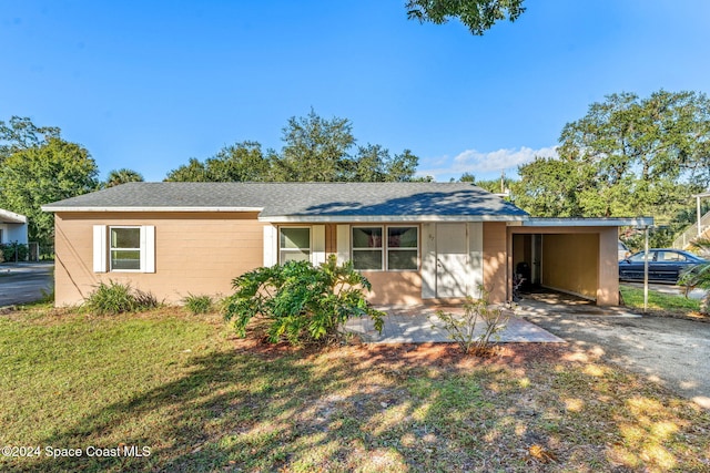 ranch-style home featuring an attached carport, driveway, concrete block siding, a front lawn, and roof with shingles