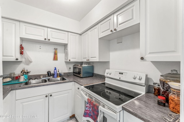 kitchen with white range with electric cooktop, a sink, stainless steel microwave, white cabinets, and dark countertops