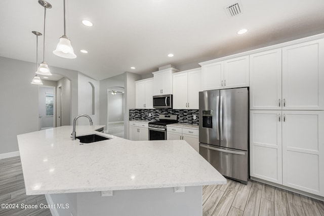 kitchen featuring a large island with sink, sink, white cabinets, decorative light fixtures, and appliances with stainless steel finishes