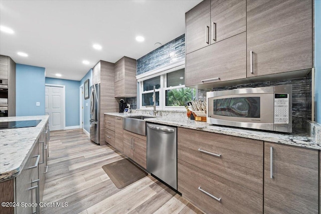 kitchen featuring sink, appliances with stainless steel finishes, tasteful backsplash, light hardwood / wood-style floors, and light stone counters