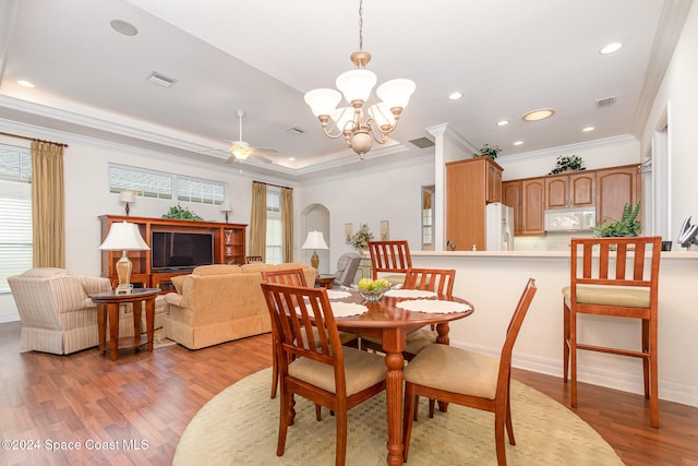 dining space featuring a raised ceiling, ornamental molding, light wood-type flooring, and ceiling fan with notable chandelier