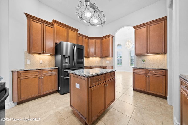 kitchen with stainless steel fridge, light stone counters, light tile patterned floors, a kitchen island, and hanging light fixtures