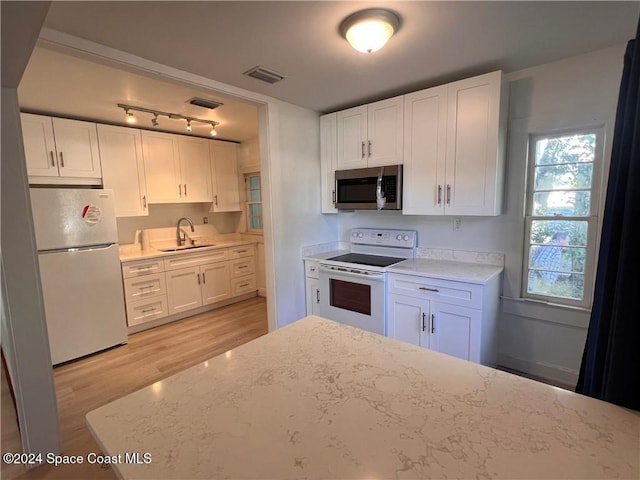 kitchen with white cabinets, light stone countertops, light hardwood / wood-style floors, sink, and white appliances