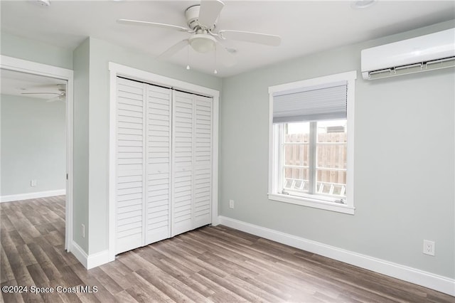 unfurnished bedroom featuring a closet, an AC wall unit, light wood-type flooring, and ceiling fan