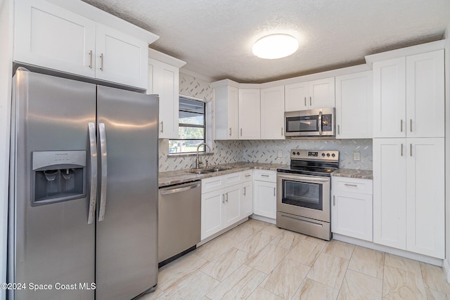 kitchen featuring light stone countertops, sink, a textured ceiling, stainless steel appliances, and white cabinets