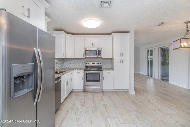 kitchen with appliances with stainless steel finishes, hanging light fixtures, white cabinets, decorative backsplash, and an inviting chandelier