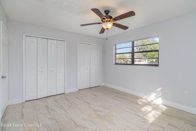 unfurnished bedroom featuring ceiling fan, a textured ceiling, and two closets