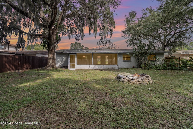 back house at dusk featuring a sunroom and a lawn