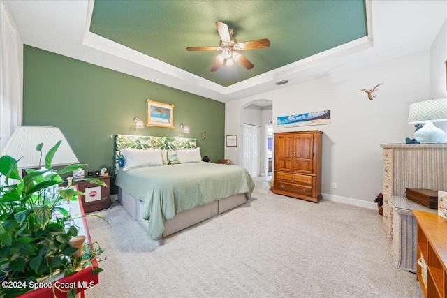 carpeted bedroom with a closet, a tray ceiling, and ceiling fan