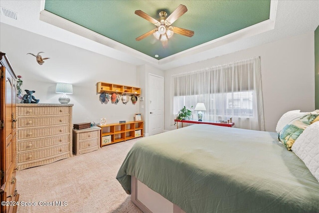 carpeted bedroom with ceiling fan, a textured ceiling, and a tray ceiling