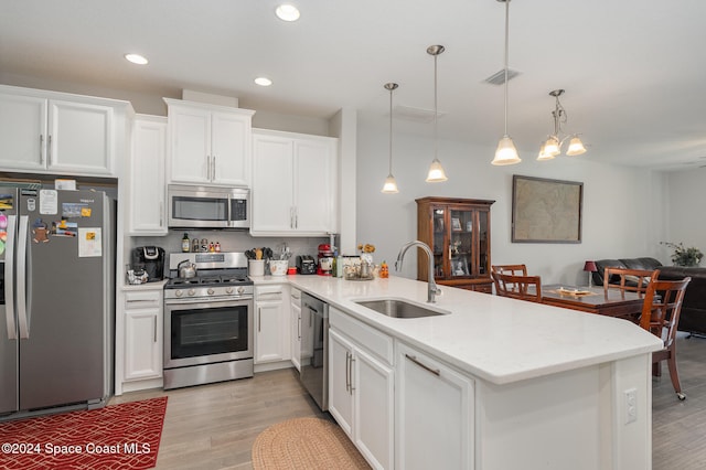 kitchen with sink, kitchen peninsula, appliances with stainless steel finishes, decorative light fixtures, and light hardwood / wood-style flooring