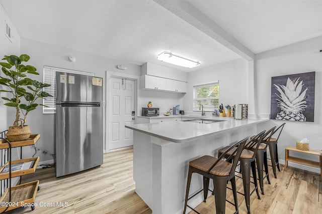 3524 S Atlantic Ave, Cocoa Beach, FL 32931 - kitchen featuring freestanding refrigerator, a peninsula, light wood-style floors, a kitchen breakfast bar, and a textured ceiling