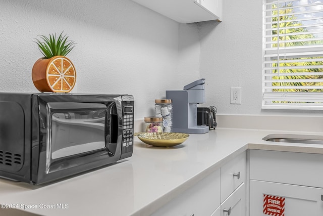 3524 S Atlantic Ave, Cocoa Beach, FL 32931 - kitchen view of black microwave, white cabinetry, light countertops, and a textured wall