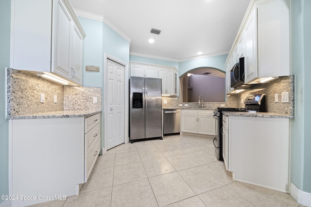 kitchen featuring tasteful backsplash, white cabinetry, light stone countertops, and appliances with stainless steel finishes