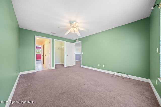 unfurnished bedroom with light carpet, a closet, a spacious closet, and ceiling fan