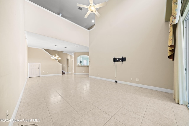 unfurnished living room with ceiling fan with notable chandelier, light tile patterned flooring, and a high ceiling