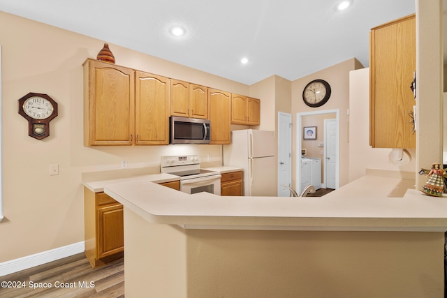 kitchen featuring white appliances, light brown cabinetry, hardwood / wood-style flooring, kitchen peninsula, and washer and dryer