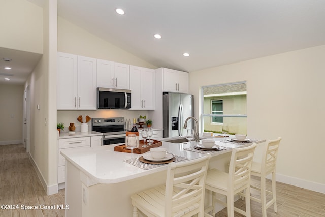 kitchen featuring a center island with sink, appliances with stainless steel finishes, a kitchen bar, vaulted ceiling, and light hardwood / wood-style floors