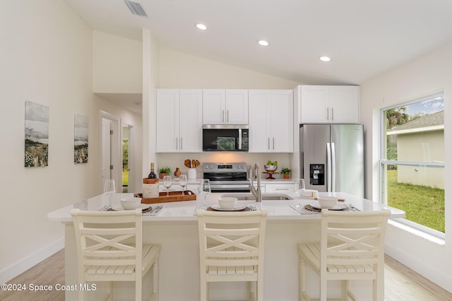 kitchen with a breakfast bar, light hardwood / wood-style flooring, appliances with stainless steel finishes, and vaulted ceiling